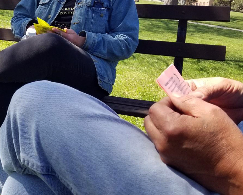 This image depicts hands holding a pink piece of paper and another person holding a yellow piece of paper, participating in the read-aloud activity.